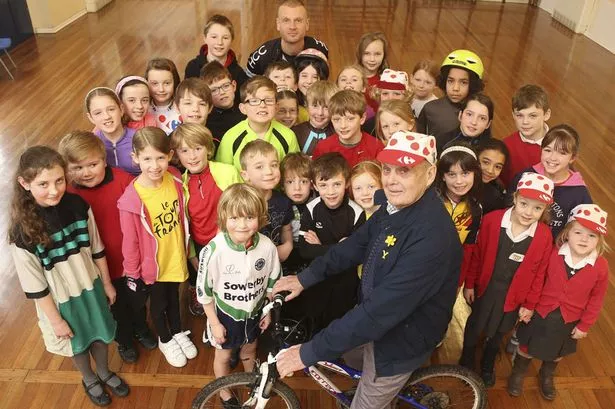 Photo: Tour de France veteran Brian Robinson meets the children of Netherthong Primary School, pictured with Mark Crouch - Deputy Head.. 